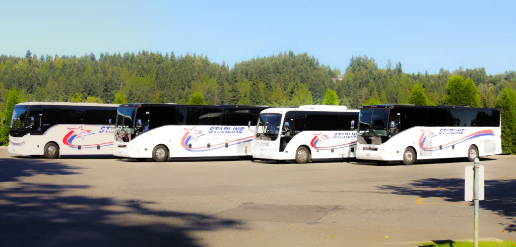 Four Starline Collection luxury charter buses parked in a row against a lush Pacific Northwest forest backdrop
