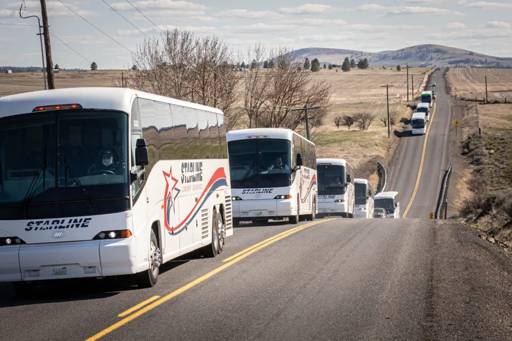 Fleet of Starline luxury charter buses traveling in convoy along a scenic Pacific Northwest highway