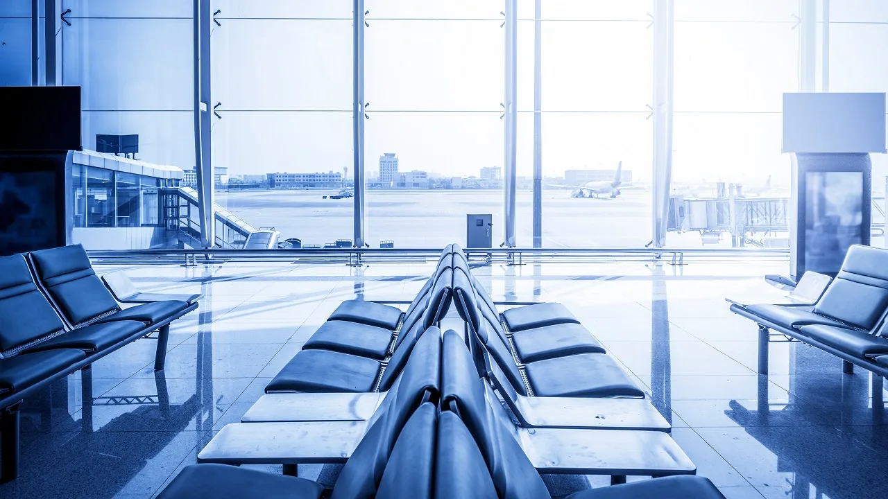 Modern airport terminal gate seating area with floor-to-ceiling windows overlooking the tarmac