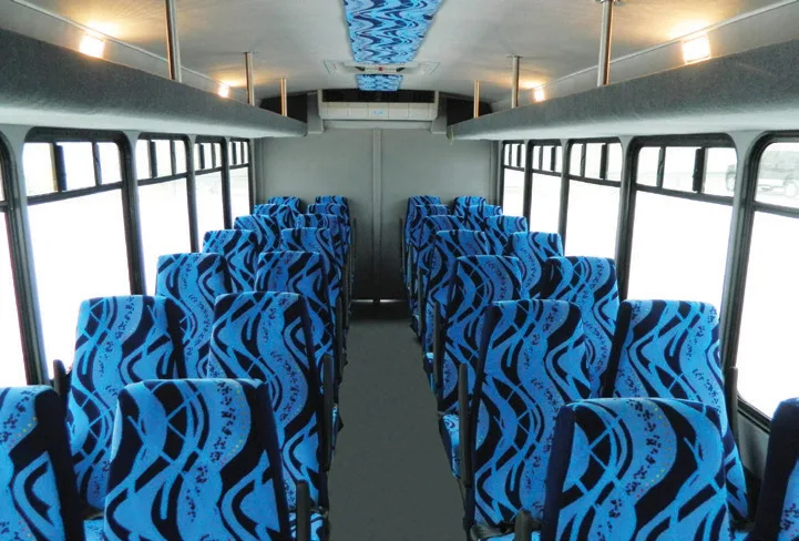 Spacious charter bus interior with rows of blue patterned seats and overhead lighting