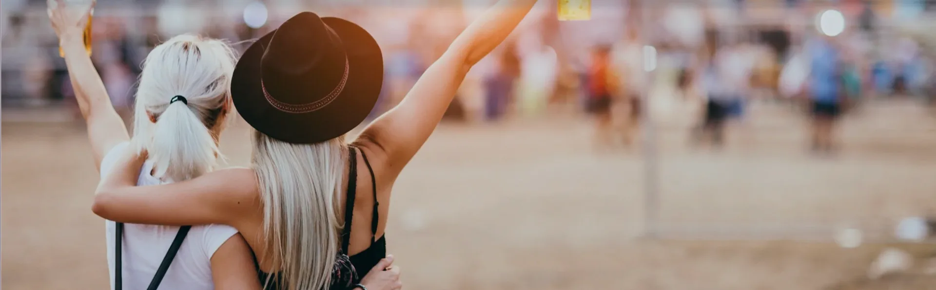 Two women with arms raised enjoying an outdoor music festival crowd