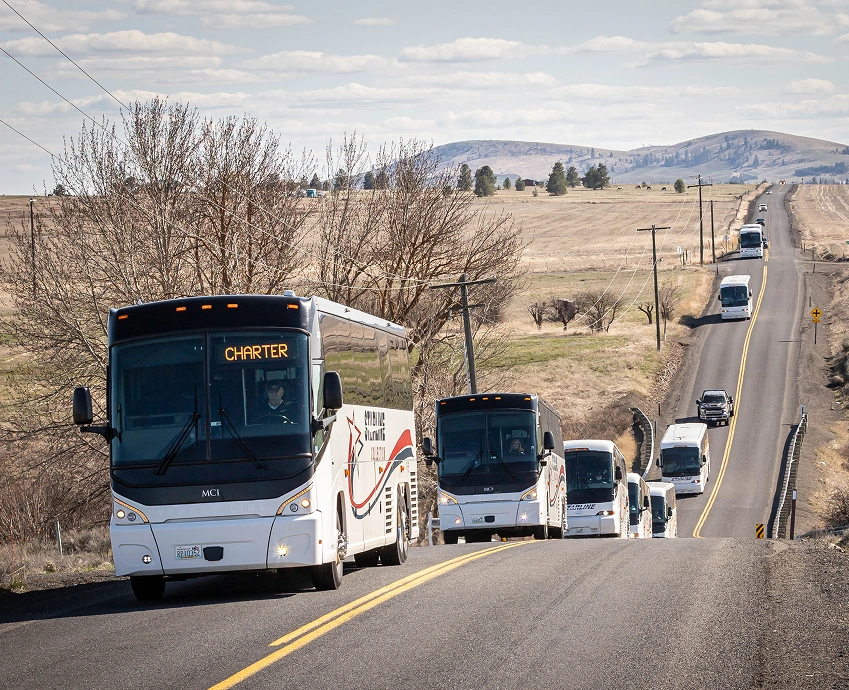 Convoy of Starline charter motorcoaches driving in a line along a rural Eastern Washington two-lane highway