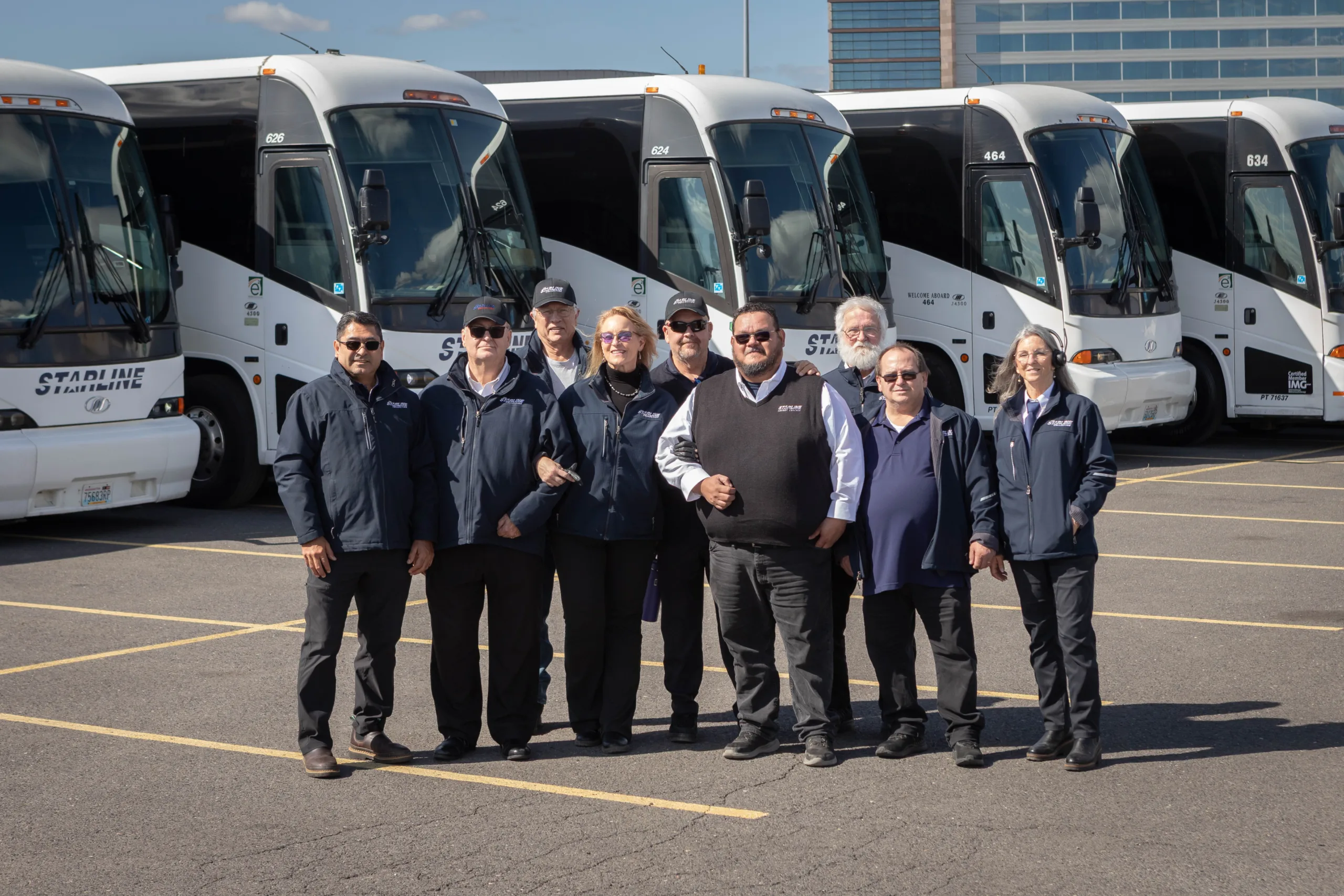 Starline Collection professional charter bus drivers and staff posing in front of luxury white motor coaches