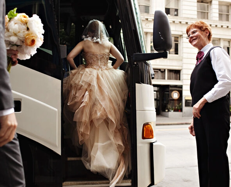Starline driver smiling as a bride in a gown boards a white motorcoach on a city street
