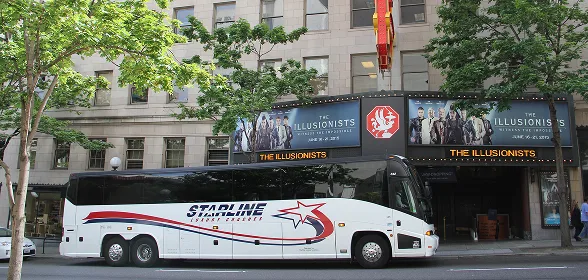 Starline luxury charter bus parked in front of The Illusionists theater marquee in downtown Seattle