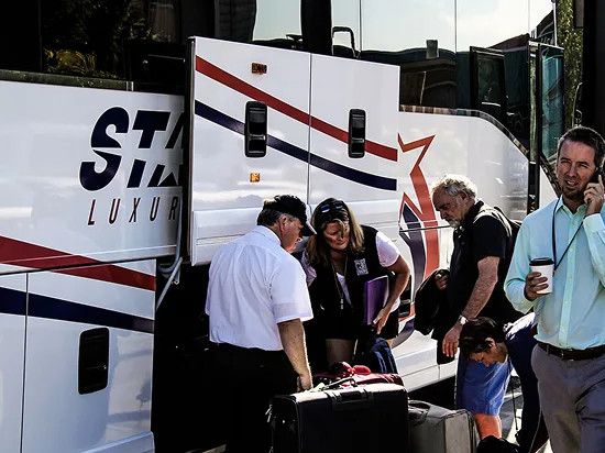 Passengers and staff loading luggage beside Starline luxury charter buses during group departure