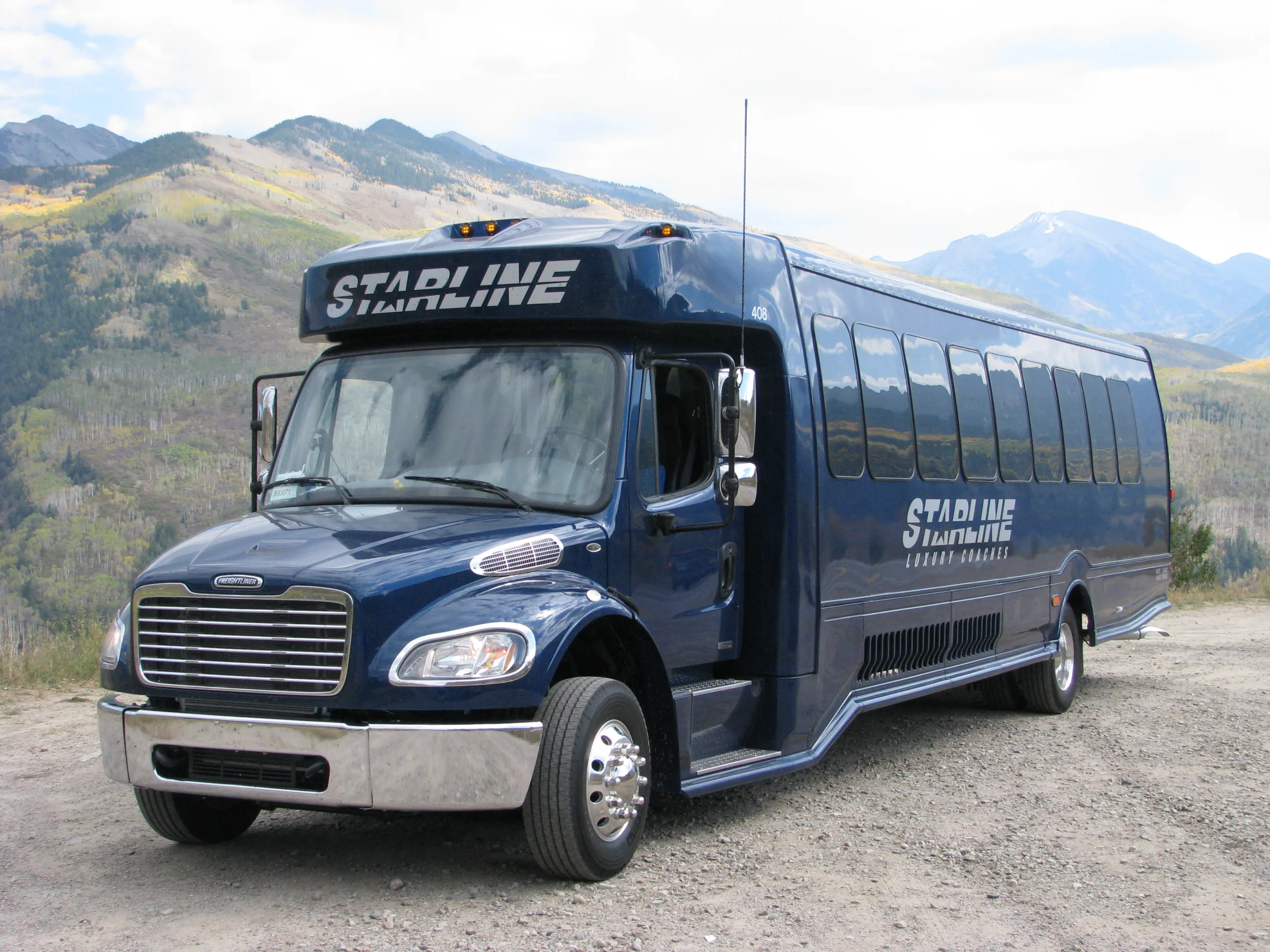 Starline Luxury Coaches navy blue charter bus parked against a scenic mountain backdrop