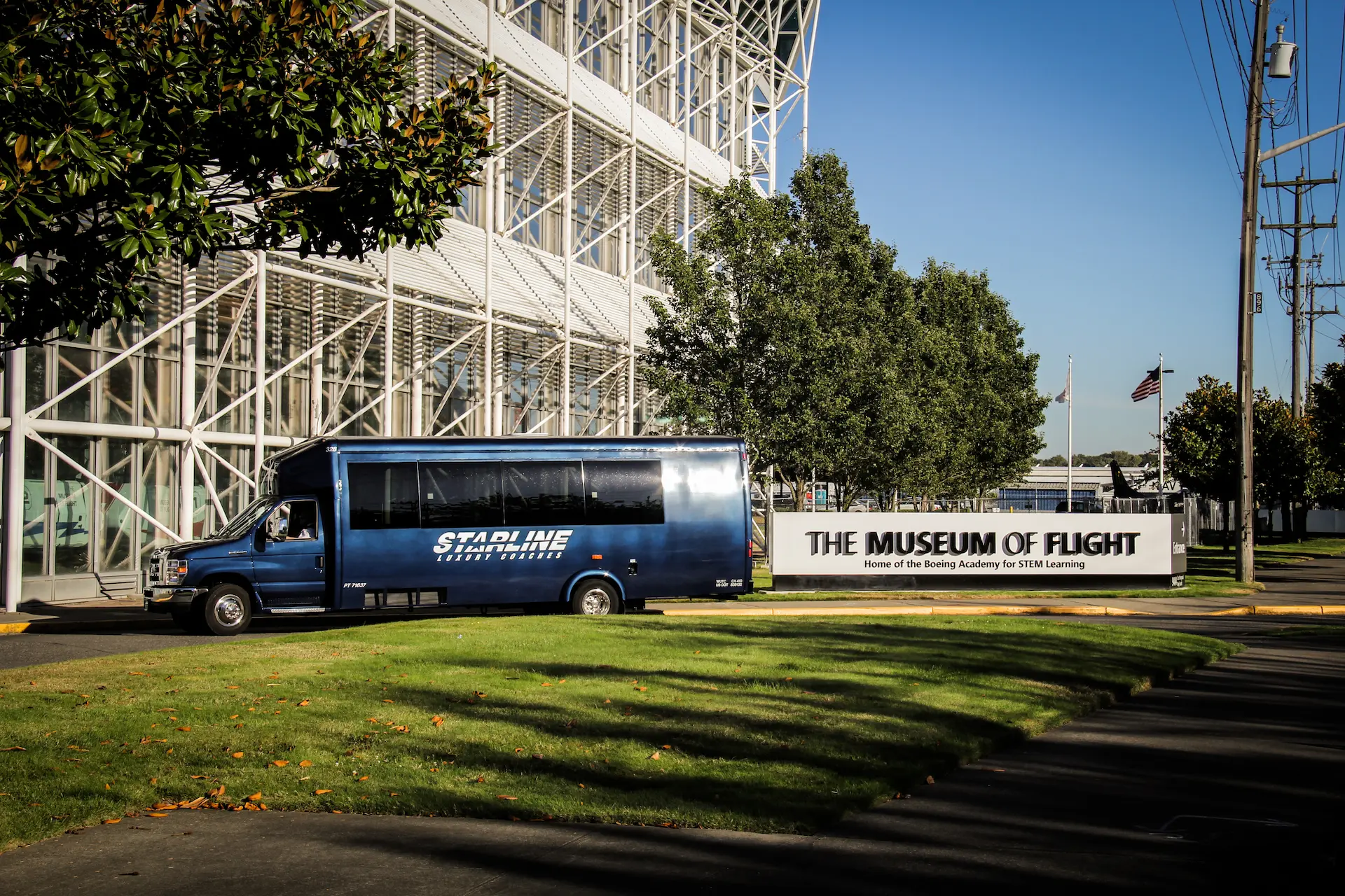 Dark blue Starline Luxury Coaches mini coach parked beside the Museum of Flight entrance sign in Seattle