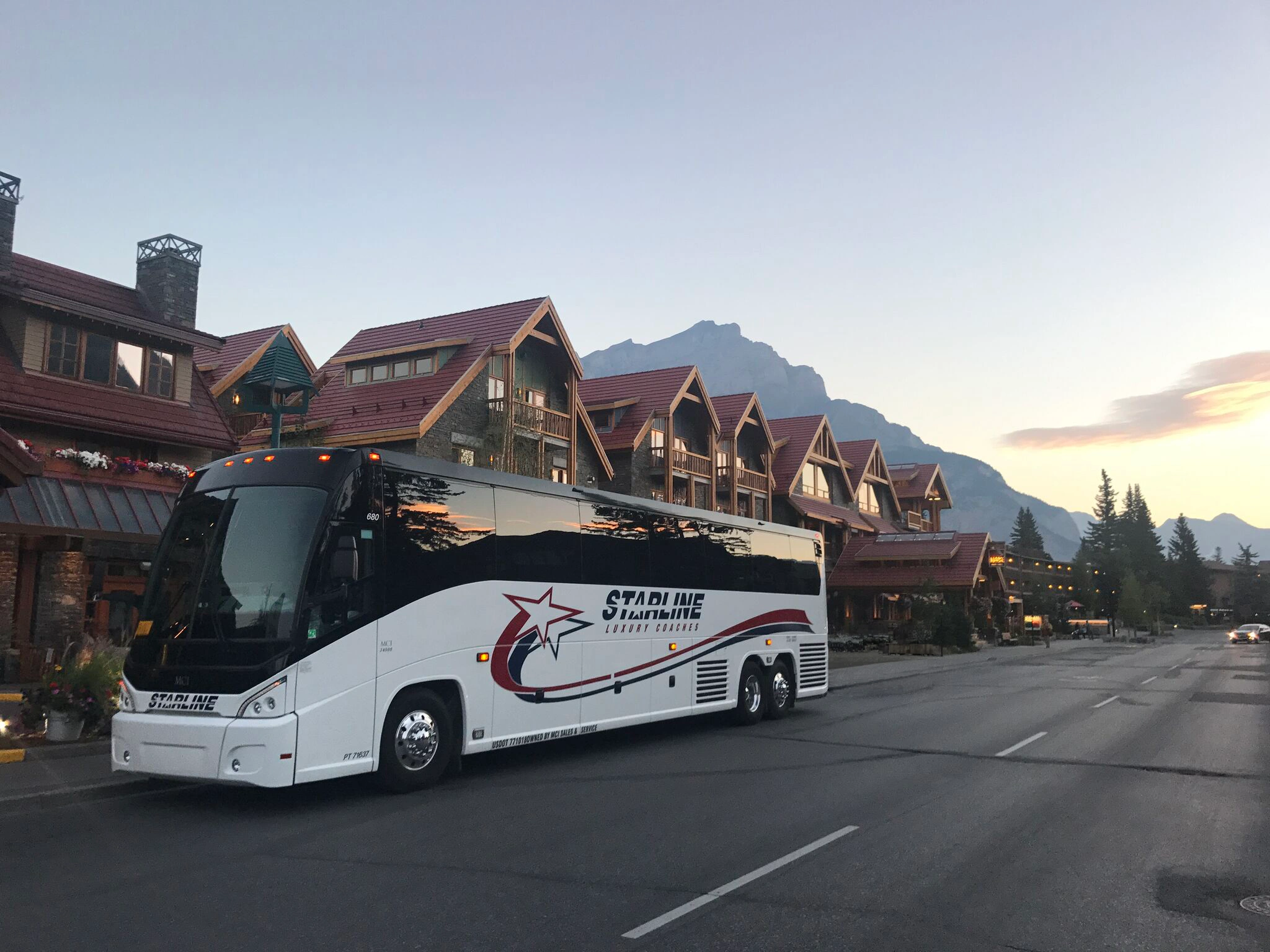 Starline Luxury Coaches motorcoach parked outside a mountain lodge resort at dusk with peaks visible in background