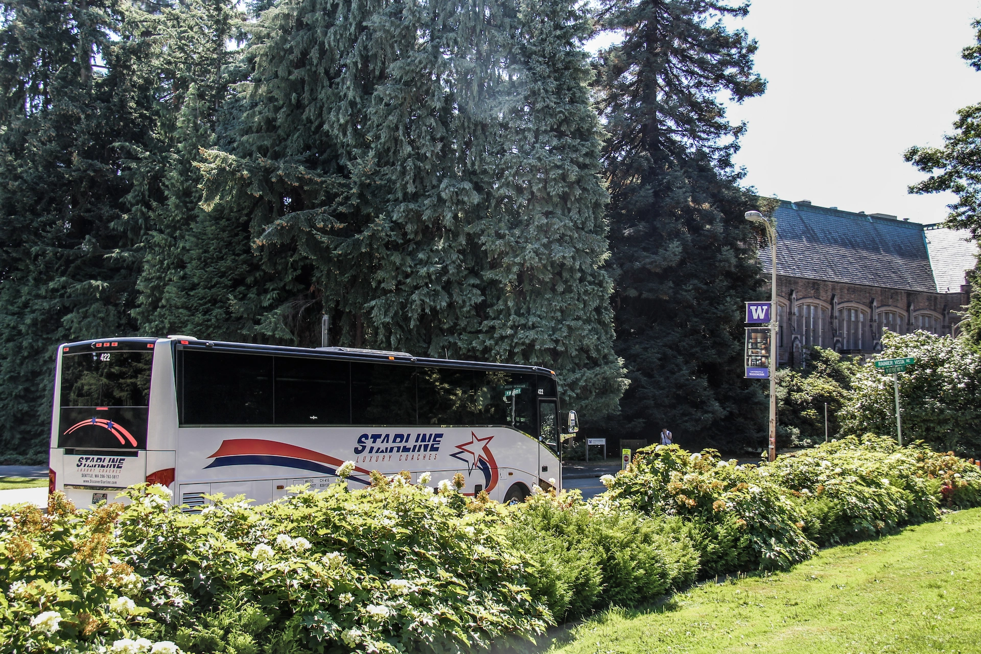 Starline Luxury Coaches motorcoach driving past University of Washington campus building and landscaped grounds