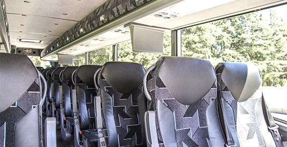 Starline motorcoach interior showing rows of black patterned fabric seats with overhead monitor and large windows