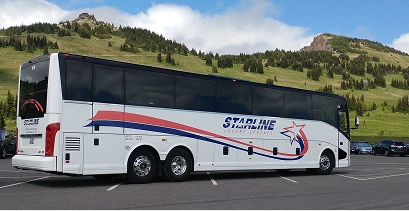 Starline motorcoach parked in a lot with a green mountain meadow and rocky butte in the background