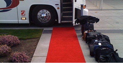 Red carpet rolled out beside a Starline motorcoach with passenger luggage lined up on the curb for loading