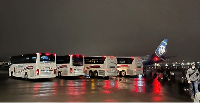 Three Starline motorcoaches staged on a rain-slicked airport tarmac at night beside an Alaska Airlines aircraft