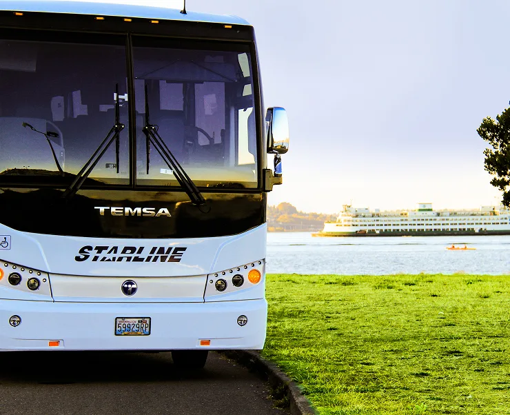 Starline luxury charter bus parked near Pacific Northwest waterfront with ferry in background
