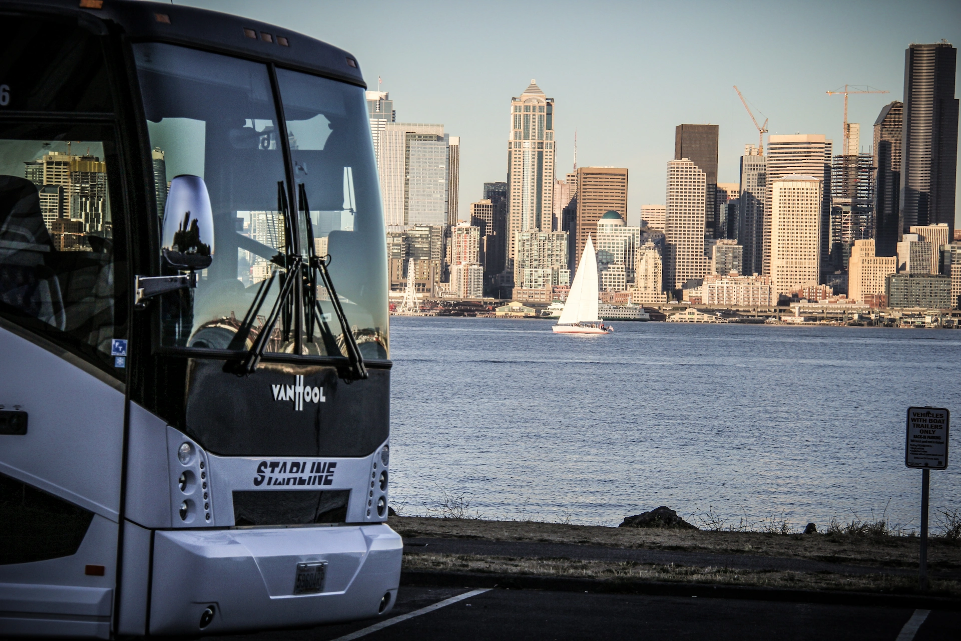 White Starline Van Hool motorcoach front parked with downtown Seattle skyline and Puget Sound in background
