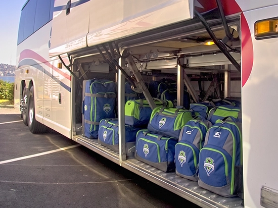 Luxury charter bus with open luggage bays loaded with Seattle Sounders team bags and equipment