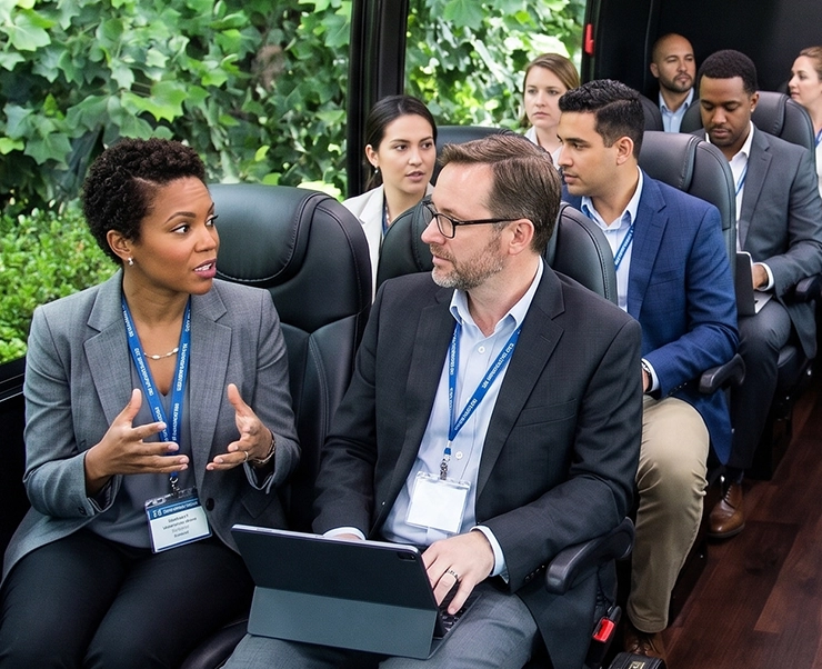 Corporate professionals in conference lanyards collaborating on a luxury charter bus with premium leather seating