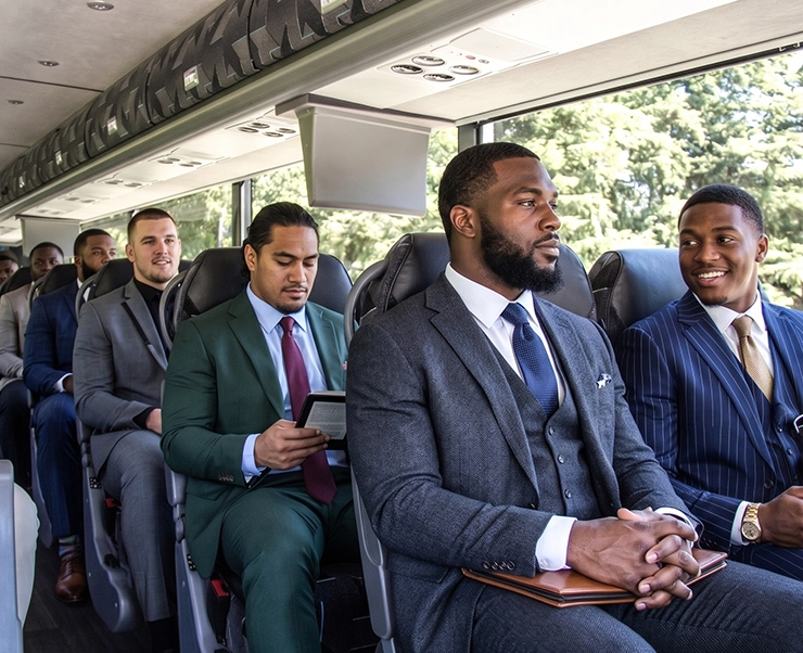 Professionally dressed men in suits seated comfortably aboard a luxury charter bus with premium leather seating