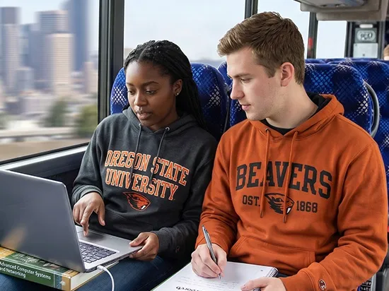 Two Oregon State University students studying on a luxury charter bus with city skyline visible through window