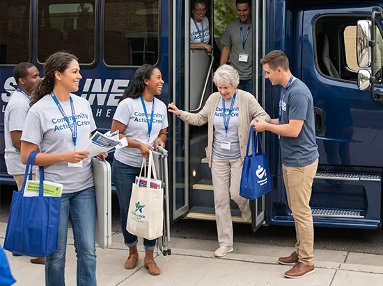 Community Action Crew volunteers assist an elderly woman boarding a Starline charter bus at a group event