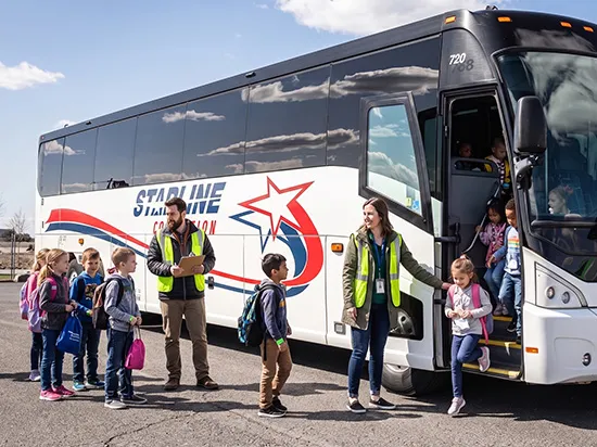 Starline Collection charter bus with staff in safety vests assisting children boarding for a school field trip