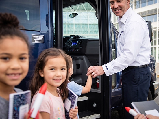 Smiling Starline driver assists young girl boarding a charter vehicle with safety check complete sign visible