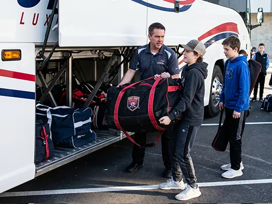 Starline chauffeur assists youth passengers loading sports bags into luxury charter bus luggage compartment