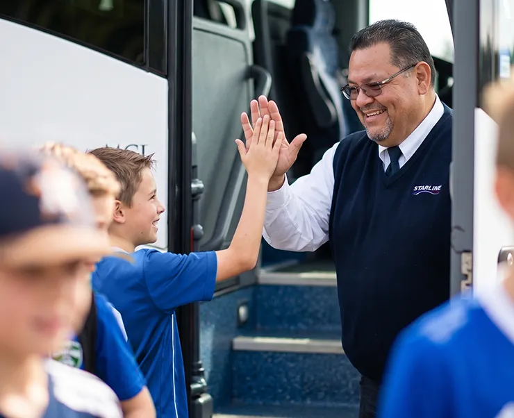 Friendly Starline driver high-fiving a young passenger boarding a charter bus