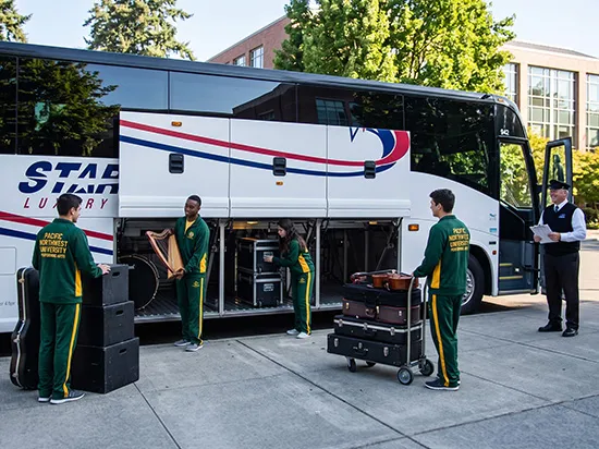 Starline Luxury charter bus driver assisting university music students loading instruments into luggage bay