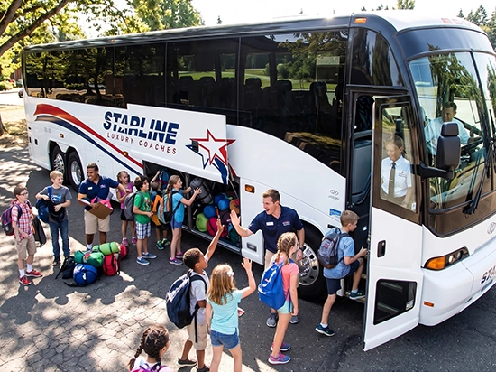 Starline Luxury Coaches staff greeting children boarding a charter bus for a school group trip
