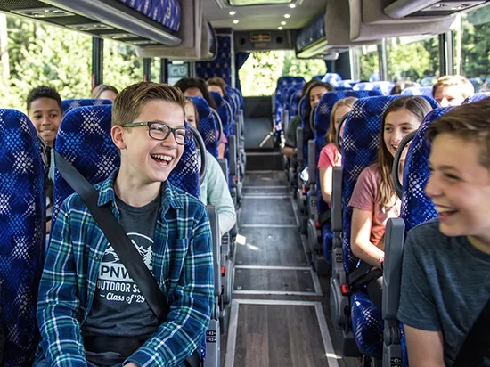 Students laughing and seated comfortably aboard a luxury charter bus with blue upholstered seats