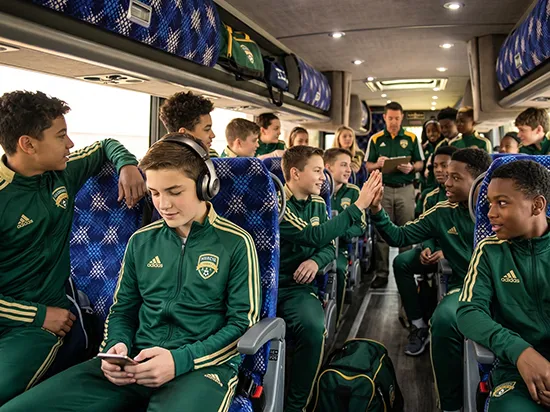 Youth soccer team in matching green Adidas uniforms seated aboard a charter bus