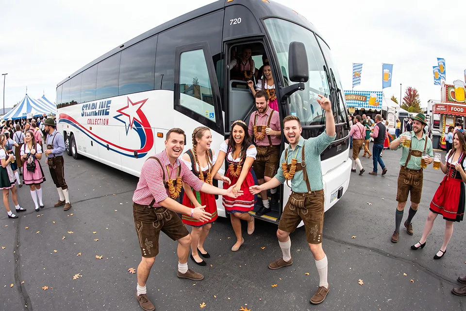 A group in traditional Oktoberfest attire celebrating outside a Starline Collection charter bus at an outdoor festival
