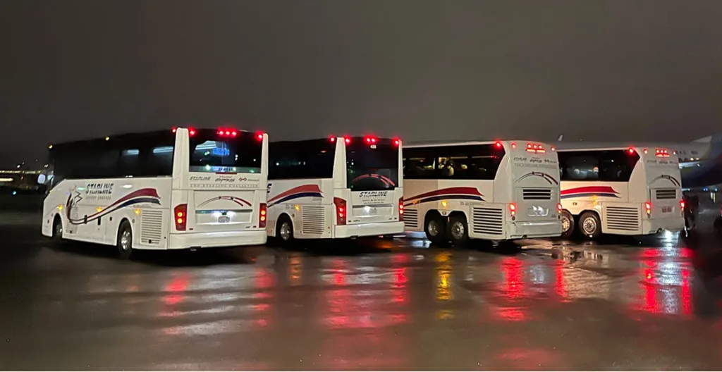 Three Starline charter buses parked on a wet tarmac at night, with red taillights reflecting on the ground