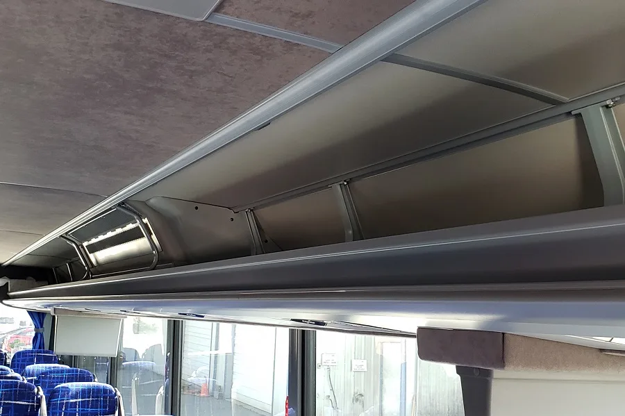 Overhead storage compartments inside a charter bus cabin, with blue passenger seats and windows visible below