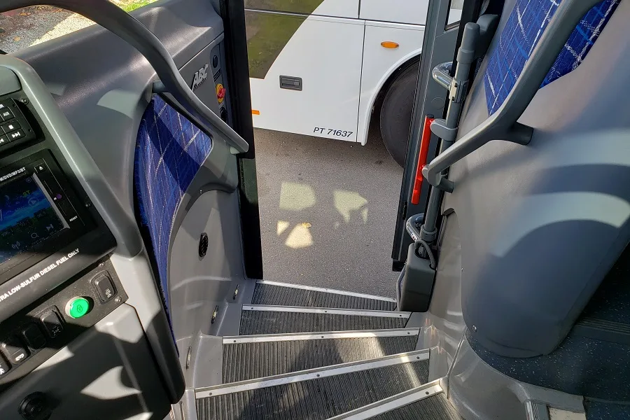 Interior view of a charter bus entrance showing the boarding steps, driver's area, and blue passenger seats