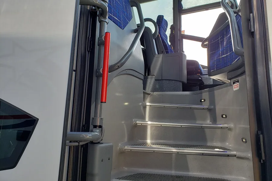 Charter bus entry steps with safety handrails leading to blue passenger seats inside the cabin