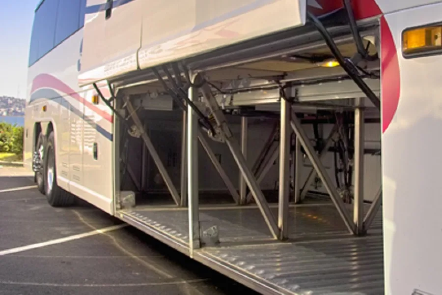 Open undercarriage luggage bay of a charter bus with a wide loading ramp extended to the ground