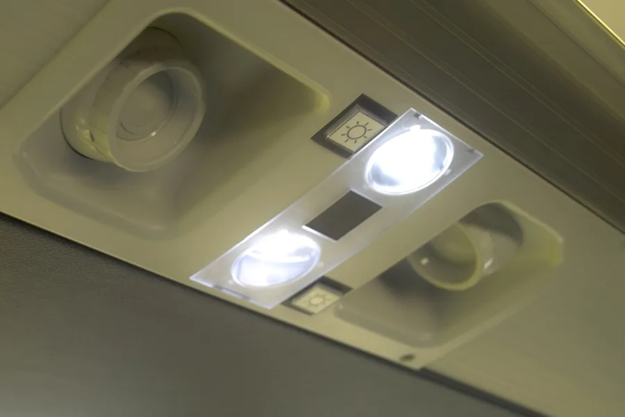 Overhead passenger cabin panel with illuminated reading lights and air vent controls on a charter bus