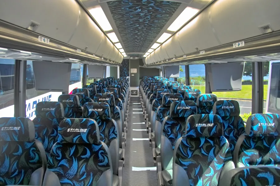 Interior of a Starline charter bus showing rows of branded, patterned seats, a center aisle, and overhead lighting