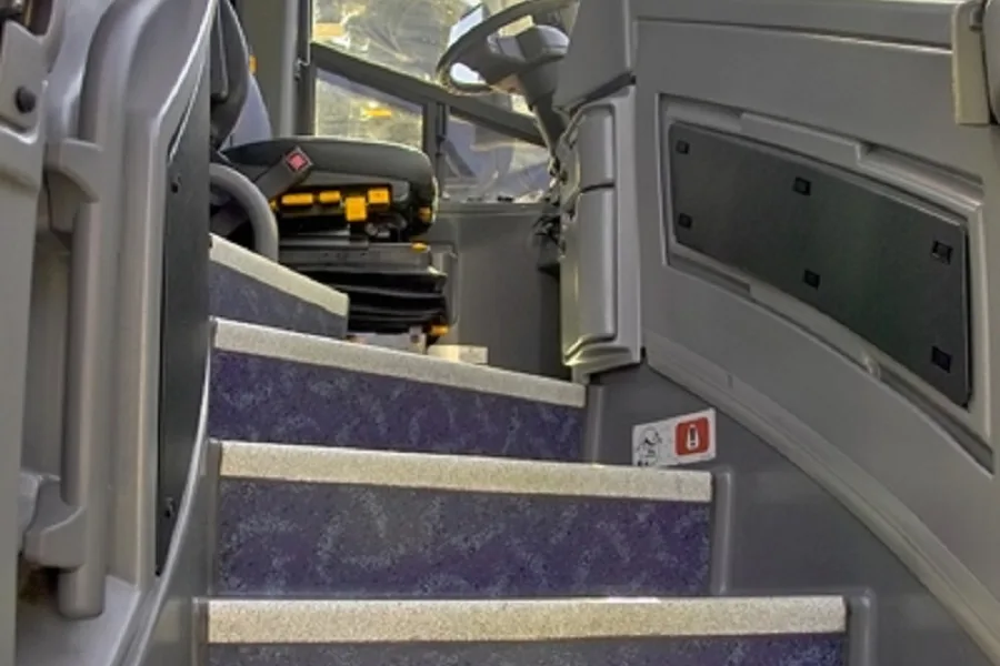 Interior stairwell and driver's area of a charter bus, showing entry steps and the driver's seat beyond