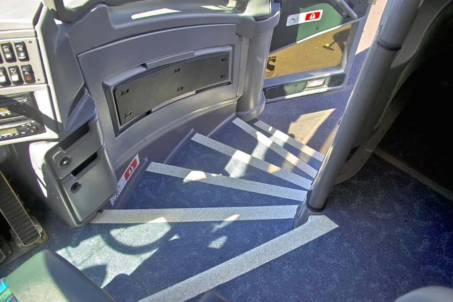 Charter bus interior showing the entry steps with anti-slip striping and blue carpeted flooring near the driver's area